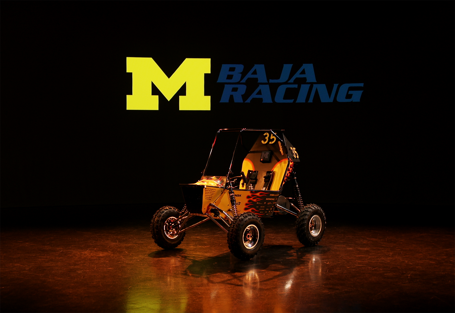 Photo of the 2025 U-M Baja race car in the video studio with Block M logo.
